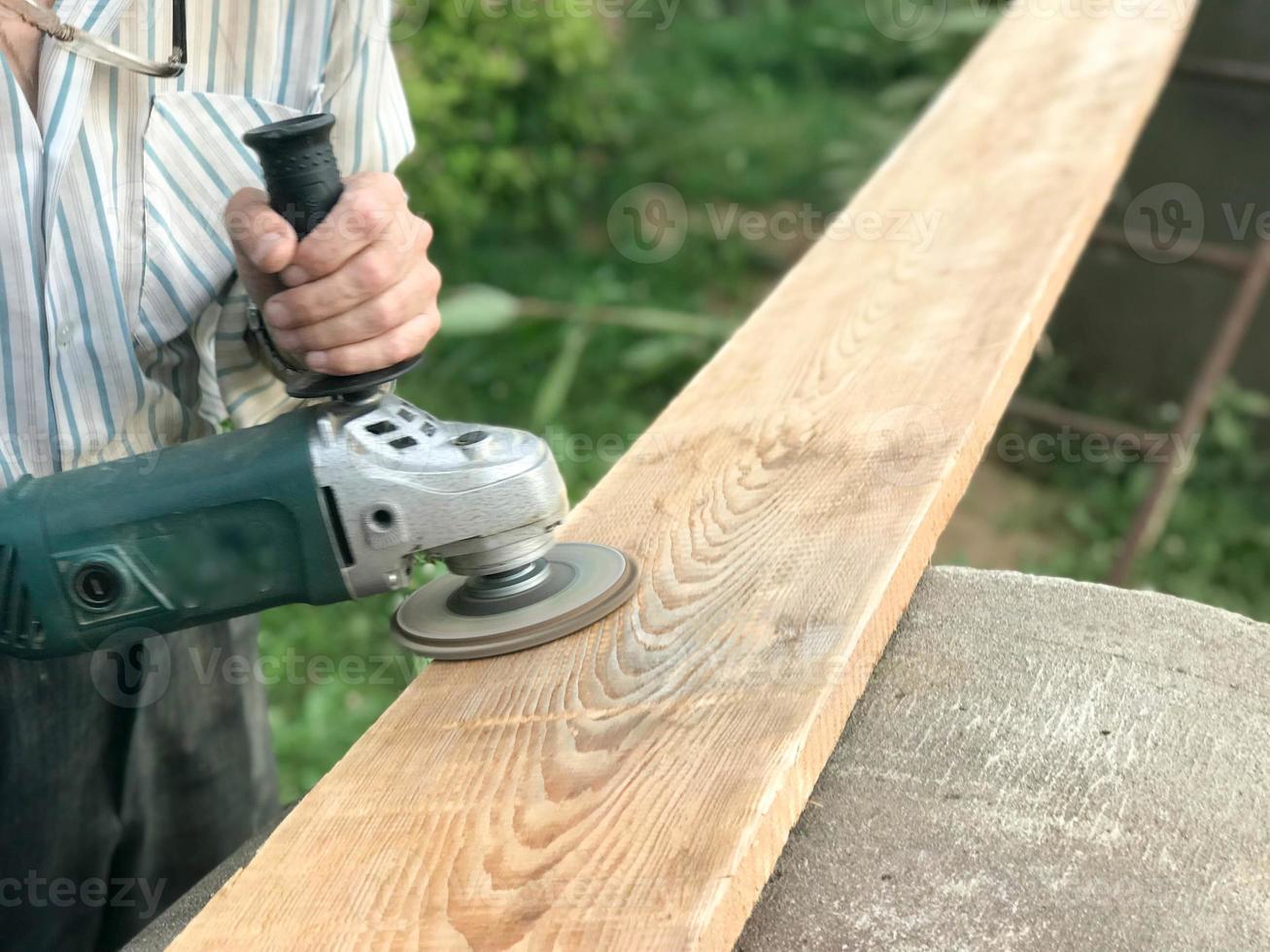 The man works with his hands, grinds the disk around for the grinder, the electric tool for grinding and polishing the surface of the wooden board photo