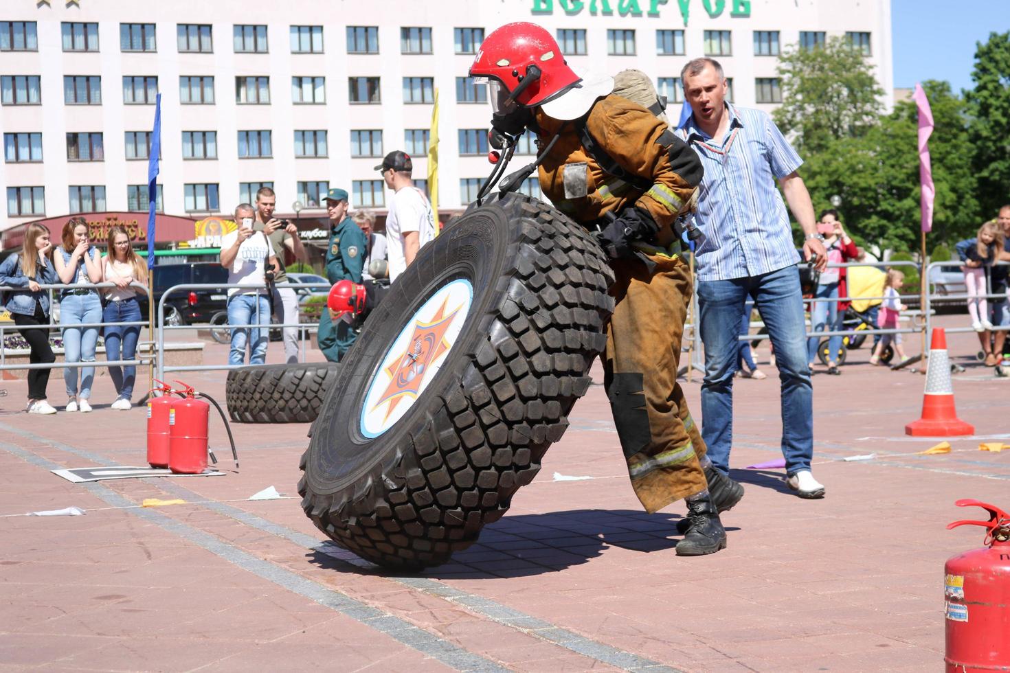 un bombero con traje ignífugo y casco corre y gira una gran rueda de goma en una competencia de extinción de incendios, bielorrusia, minsk, 08.08.2018 foto