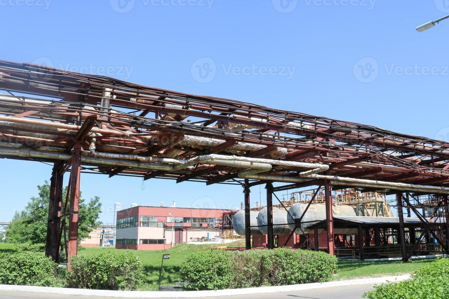 A large metallic iron pipeline trestle with pipes and wires for electricity in a petrochemical chemical refinery in the background of shell-and-tube heat exchangers and equipment photo