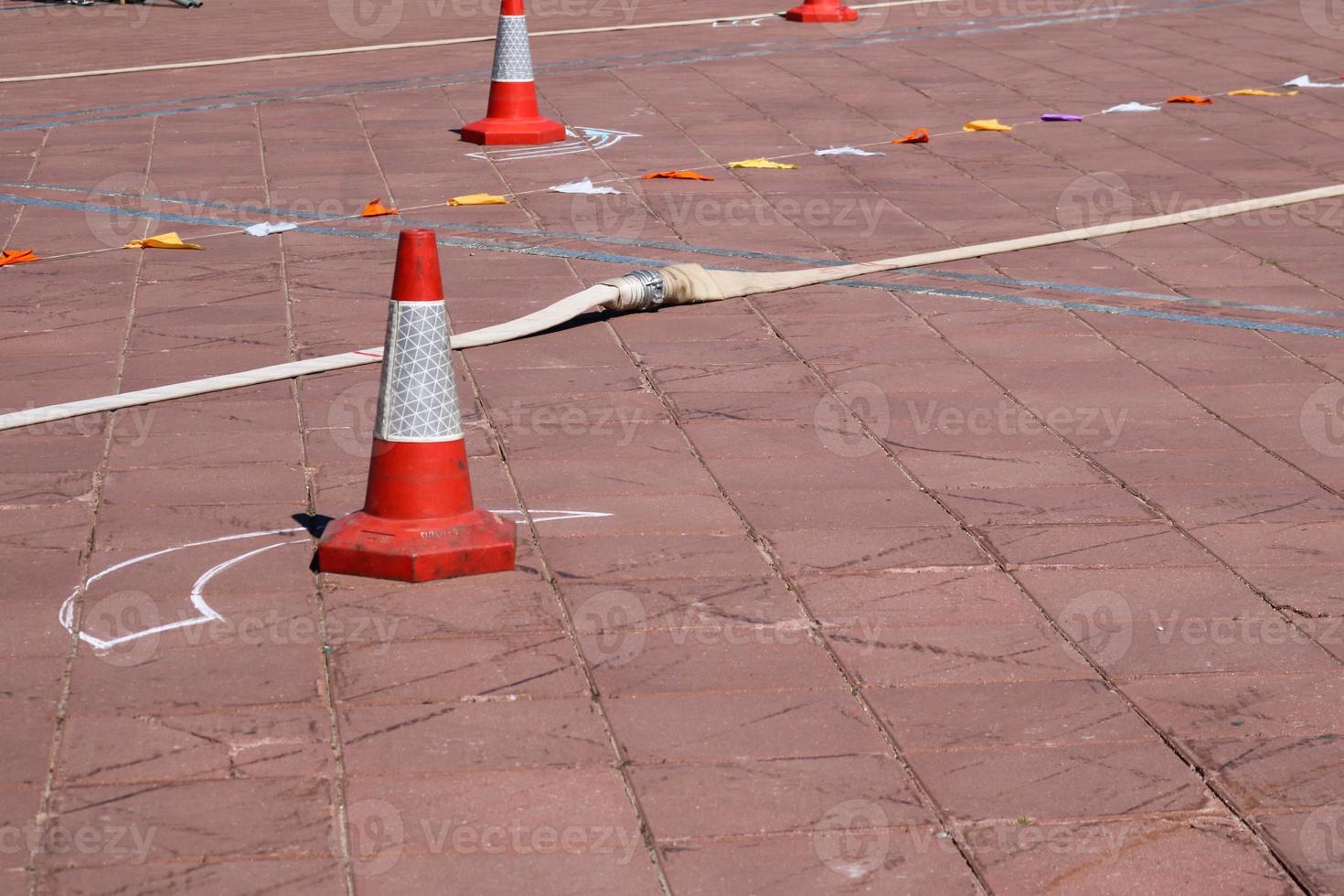 un cono naranja triangular de emergencia que denota peligro y una manguera contra incendios yacen en el suelo de piedra, la carretera. foto