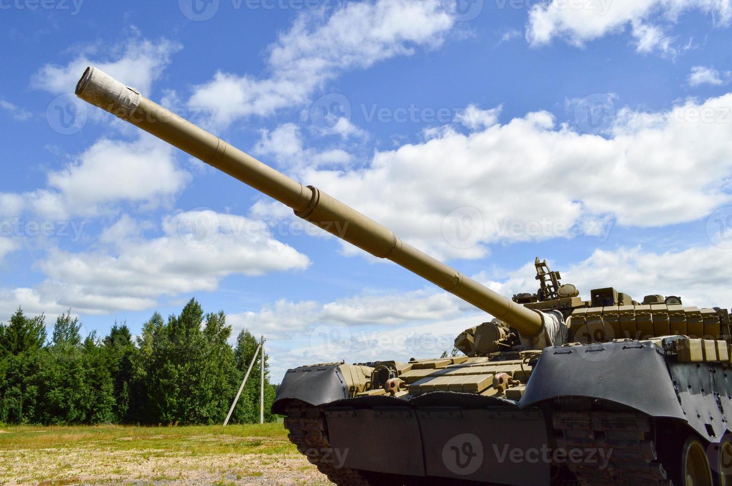 A large green military metal armored deadly dangerous iron Russian Syrian battle tank with a gun turret and a goose is parked parked against a blue sky and clouds outside the city photo