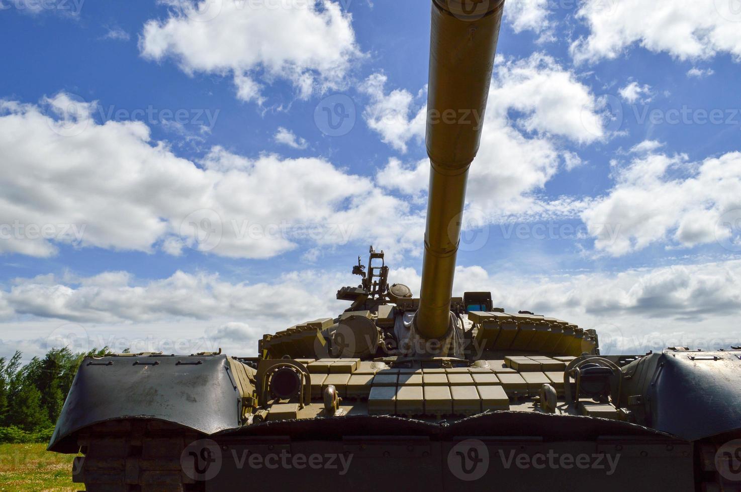 A large green military metal armored deadly dangerous iron Russian Syrian battle tank with a gun turret and a goose is parked parked against a blue sky and clouds outside the city photo