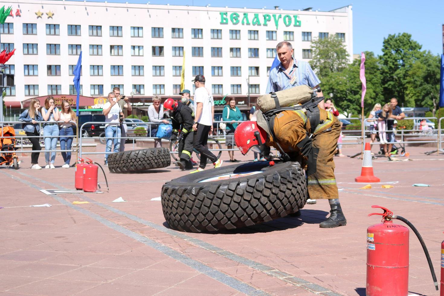 un bombero con traje ignífugo y casco corre y gira una gran rueda de goma en una competencia de extinción de incendios, bielorrusia, minsk, 08.08.2018 foto