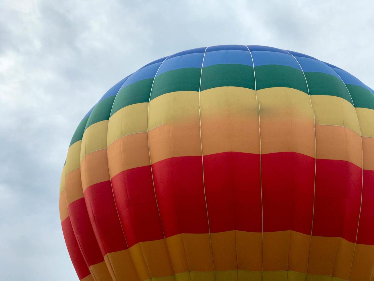 Large multi-colored bright round rainbow colored striped striped flying balloon with a basket against the sky in the evening photo