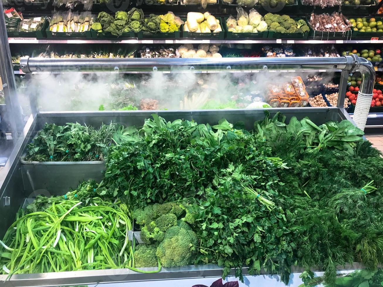 verde, verde, fresco, respetuoso con el medio ambiente, de plantas de perejil, ensalada de eneldo, cebollas de rúcula y otros alimentos vegetales se encuentra en un refrigerador moderno en una tienda de supermercado en el mostrador. el fondo foto