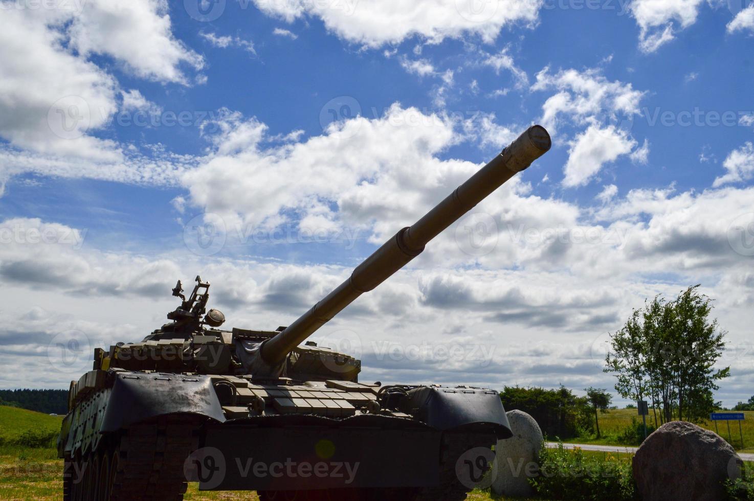 A large green military metal armored deadly dangerous iron Russian Syrian battle tank with a gun turret and a goose is parked parked against a blue sky and clouds outside the city photo