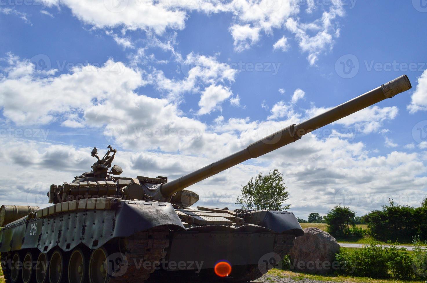 A large green military metal armored deadly dangerous iron Russian Syrian battle tank with a gun turret and a goose is parked parked against a blue sky and clouds outside the city photo