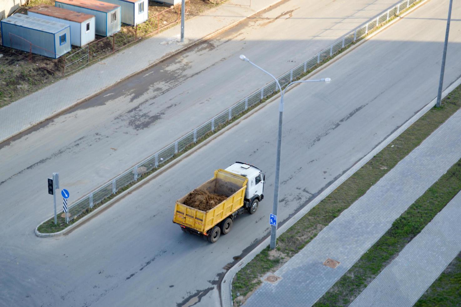 A large dump truck rides to a construction site and carries sand along an asphalt road. View from above photo