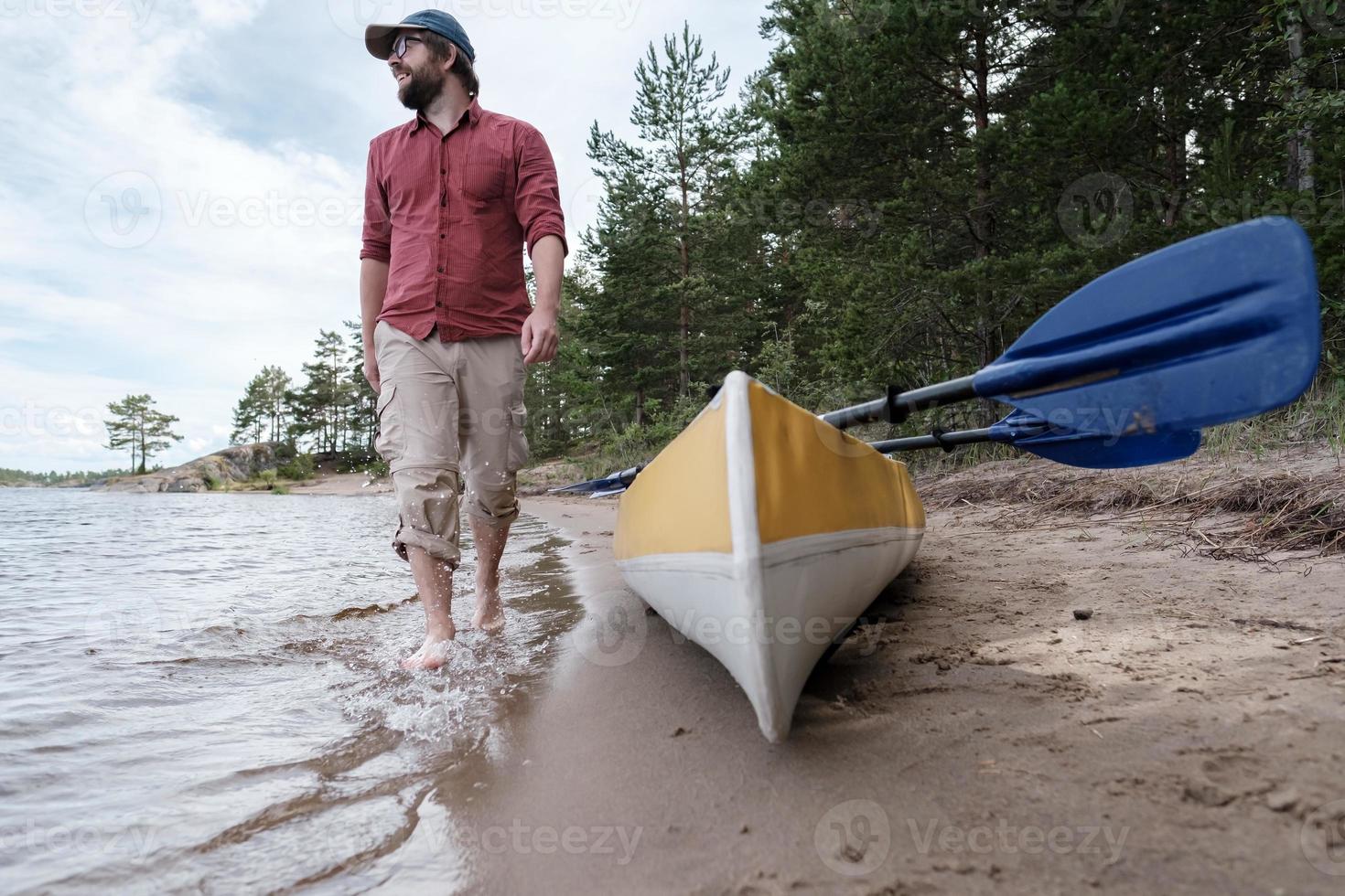 A happy, smiling man parked his kayak and walks barefoot on the water of the lake, enjoying the beautiful views. photo