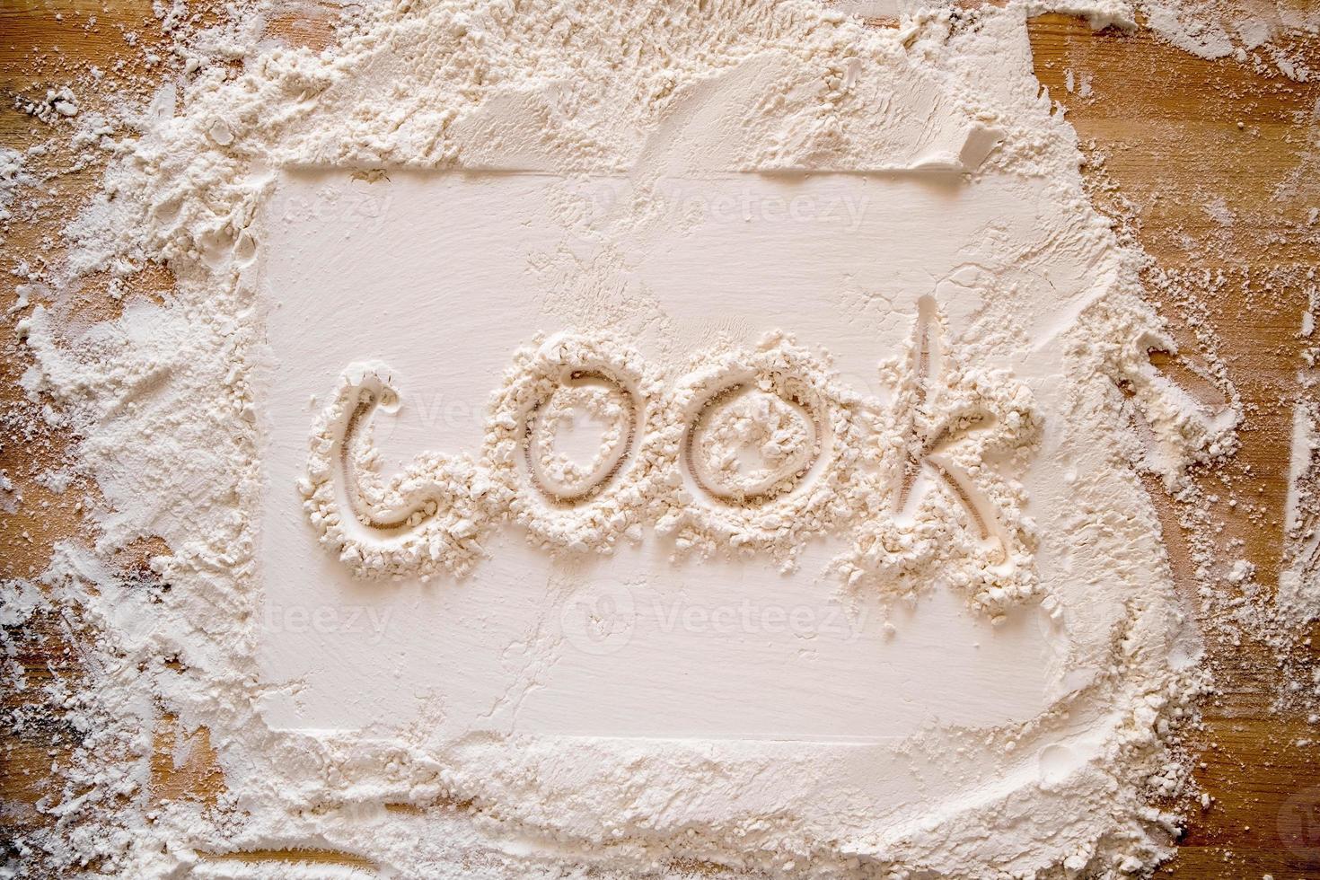 The handwritten word cook is written on flour sprinkled on a wooden table and a rectangular print. photo