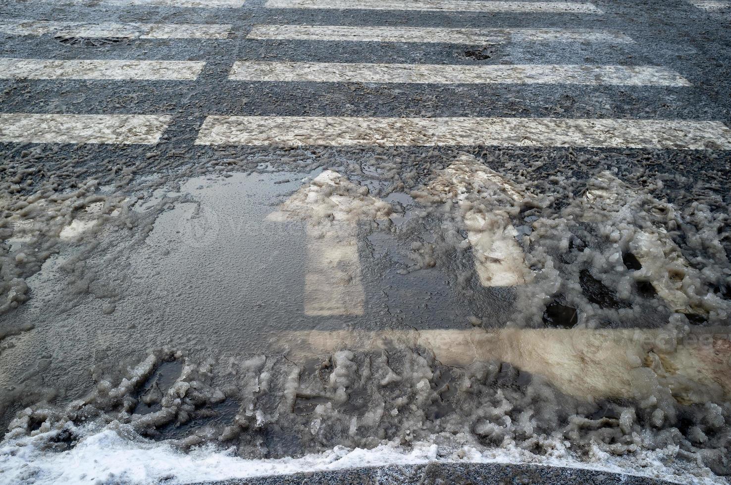 Crosswalk with arrows indicating traffic, for safety on the road. Pedestrian crossing and highway markings in the dirty melting snow. photo