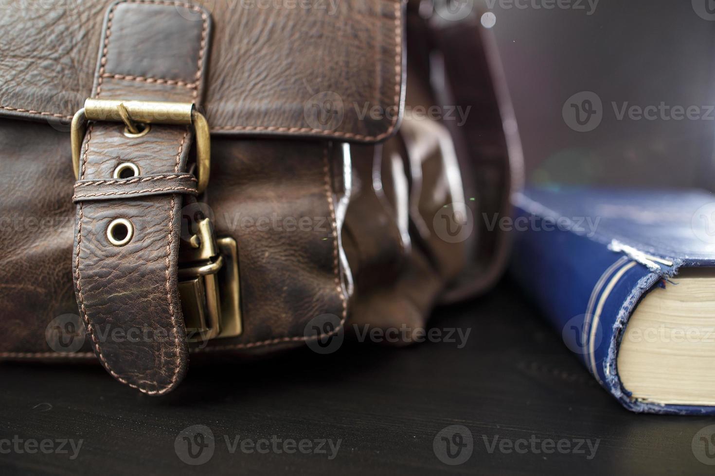 Old leather briefcase with metal buckles and a closed book lying on the table. Education concept. photo