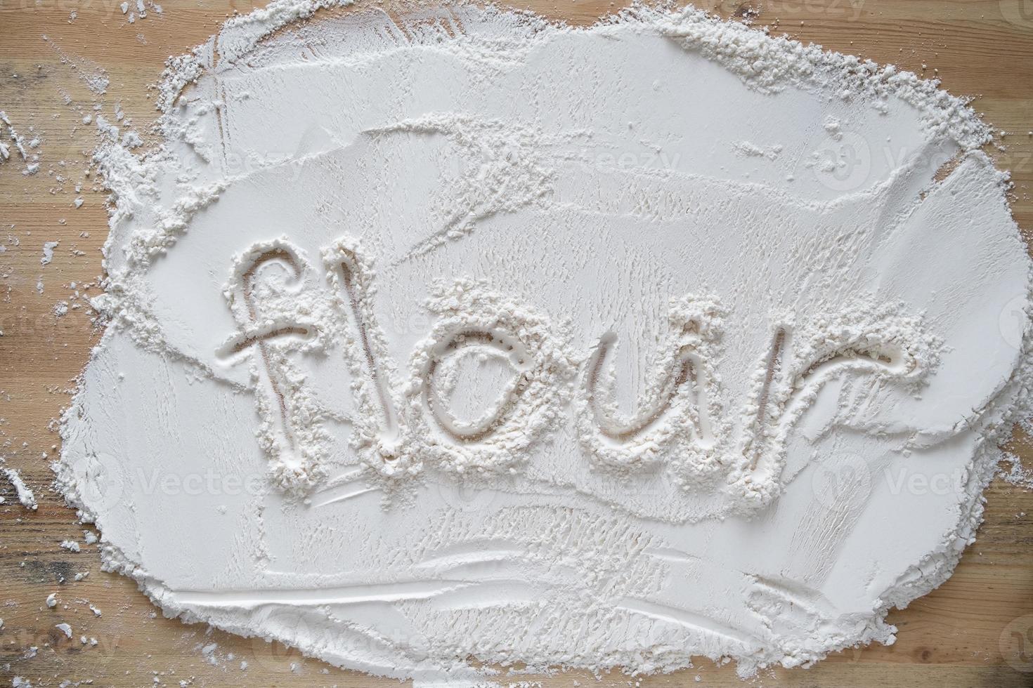 The handwritten word flour is written on milled, sifted wheat sprinkled on a wooden table. photo
