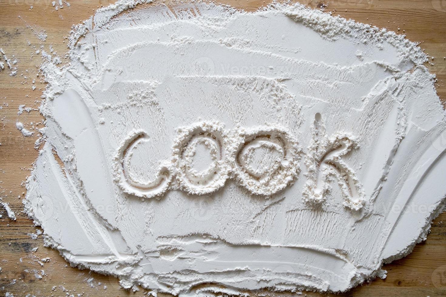 The handwritten word cook is written on flour sprinkled on a wooden table. photo