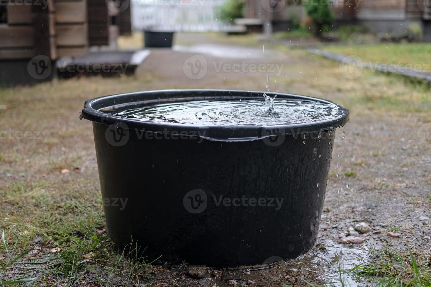 Rainwater is collected in a basin of standing under the gutter, in the yard, on a summer day. photo