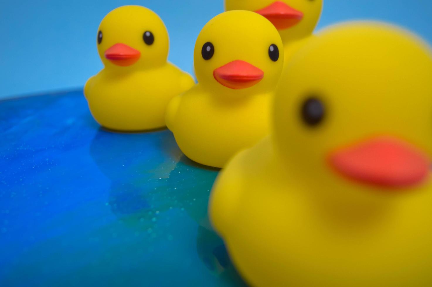 hermosos patos de juguete de bañera de goma amarilla nadan en un fondo de agua azul foto