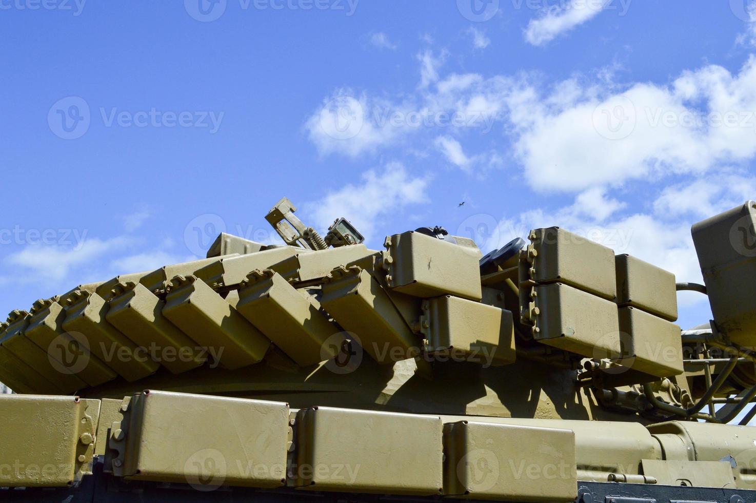 A large green military metal armored deadly dangerous iron Russian Syrian battle tank with a gun turret and a goose is parked parked against a blue sky and clouds outside the city photo