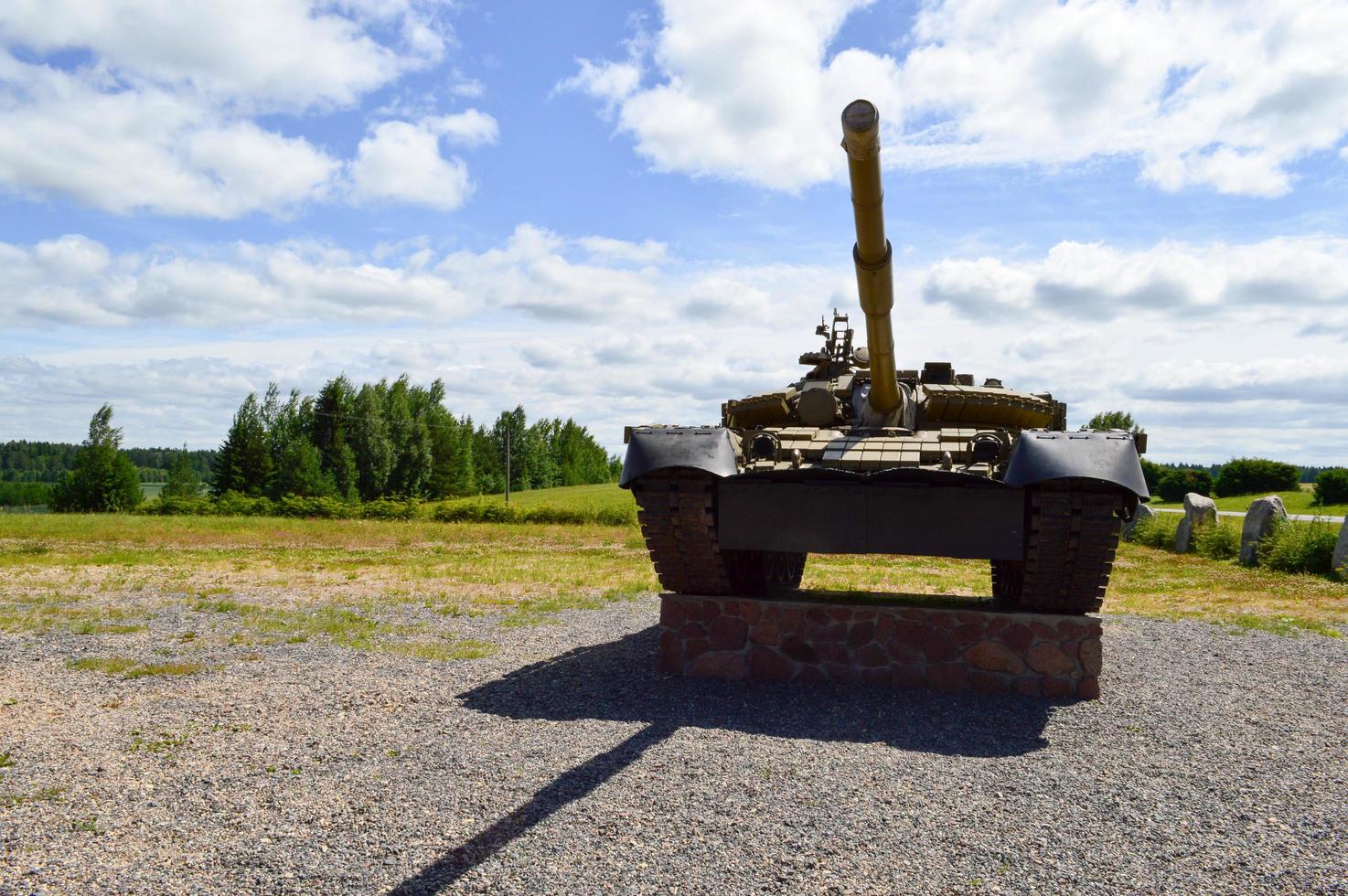 A large green military metal armored deadly dangerous iron Russian Syrian battle tank with a gun turret and a goose is parked parked against a blue sky and clouds outside the city photo