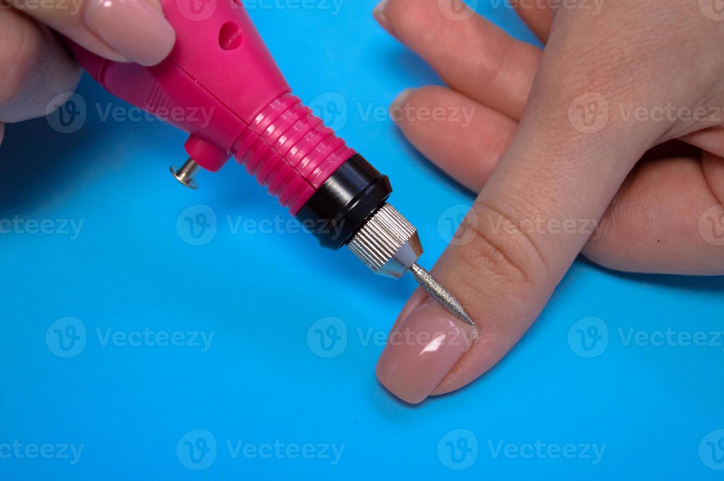 The process of making a beautiful manicure on the fingers of a finger processing a nail with a special machine in a nail beauty salon on a blue background photo
