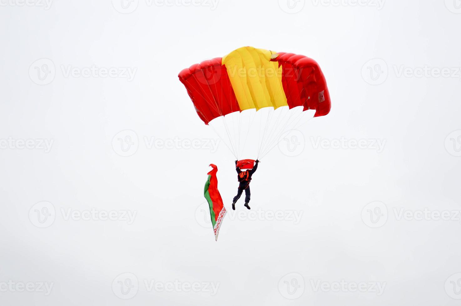 A parachutist with a bright multicolored parachute flies across the sky with the flag of the Republic of Belarus skydiver in the background of the blue sky photo