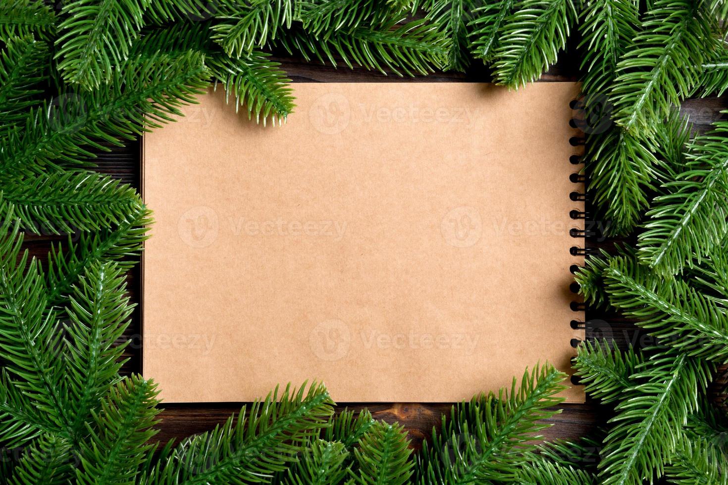 Top view of notebook made of craft paper decorated with a frame made of fir tree on wooden background. New Year time concept photo