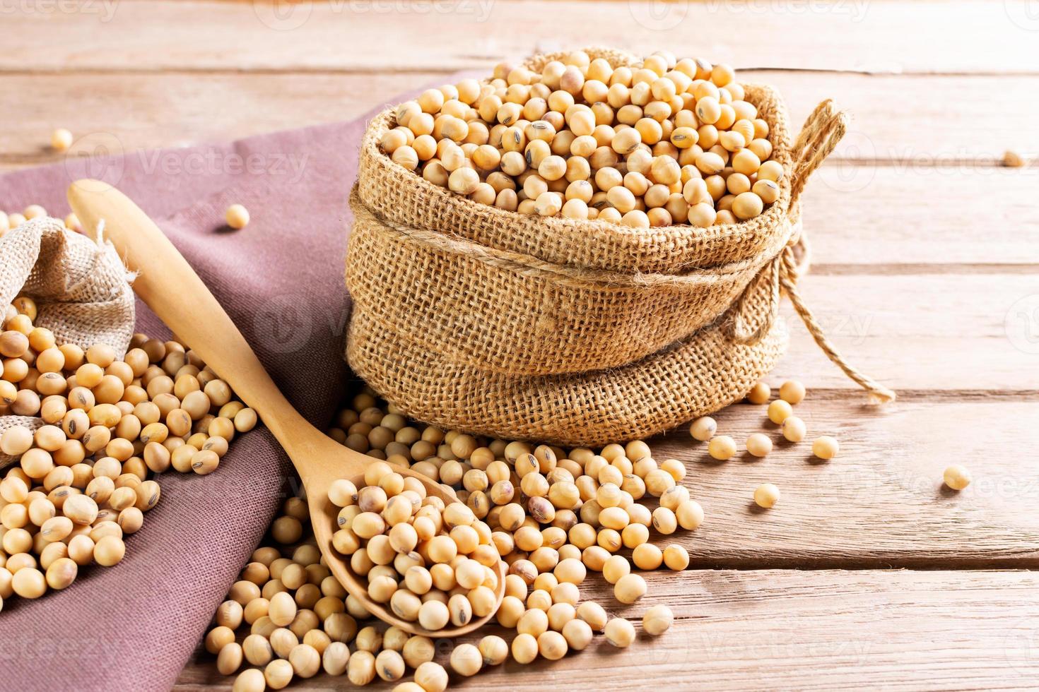 Soybean seeds in a sack with wooden spoon, placed on a wooden table, natural healthy food - top view. photo