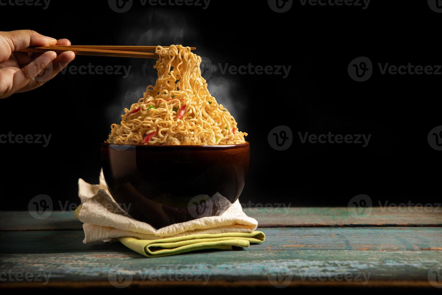 Bow of Hot Boiled Instant Noodles on the Table. Hand Using Chopsticks to Eating Noodles with Stream. Cheap Fast food Concepts. Side View with more Copy Space photo