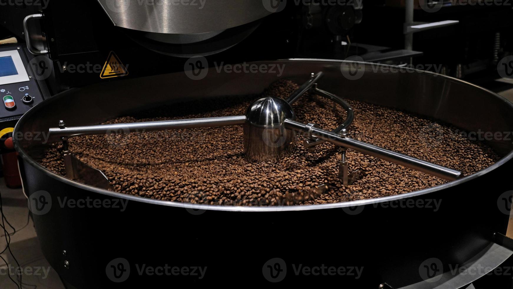 Coffee roaster machine at coffee roasting process. Mixing coffee beans. Roasted spinning cooler professional machines and fresh brown coffee beans movement close-up dark photo at factory.