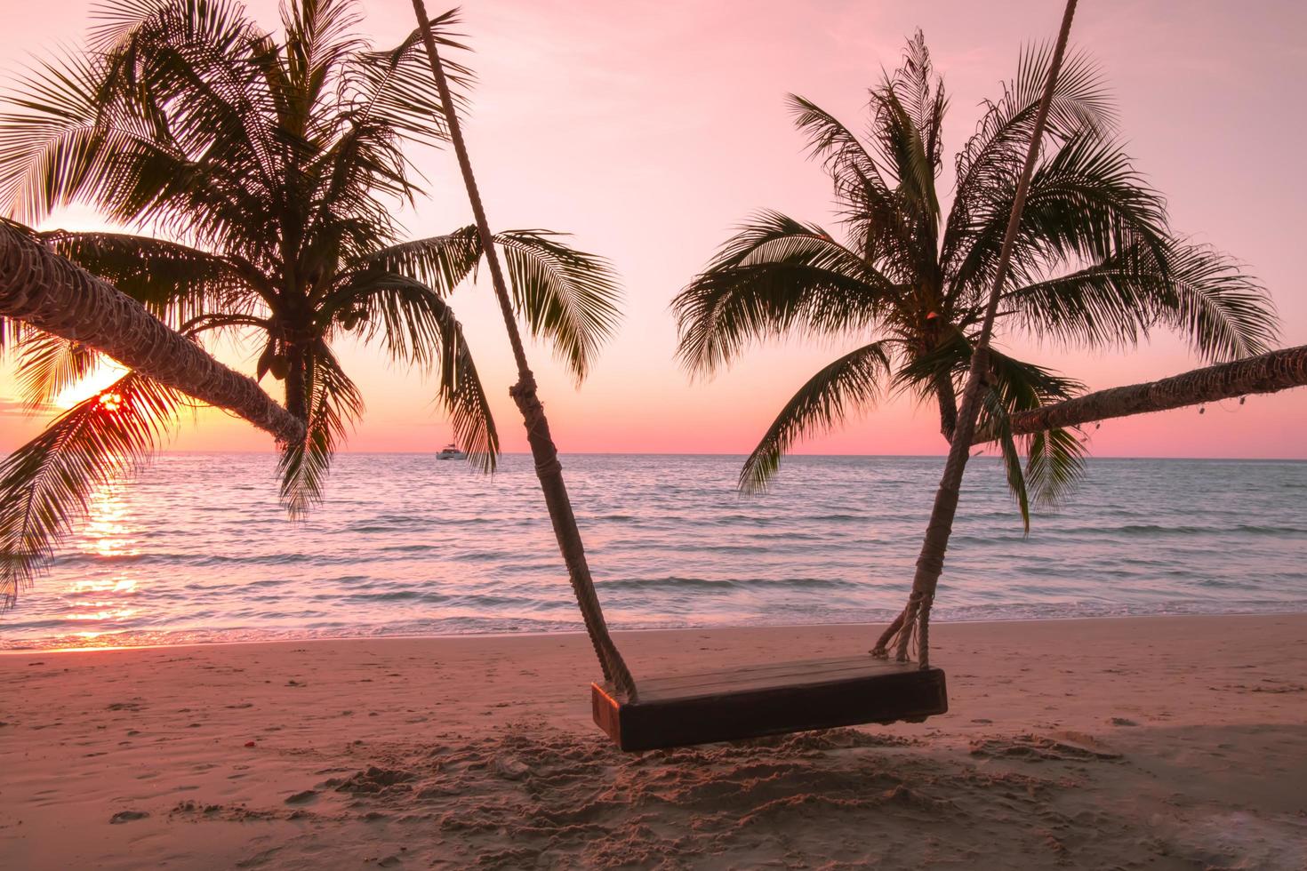 Wood swing with palm tree on the tropical beach sunset over the sea for travel in holiday relax time, photo