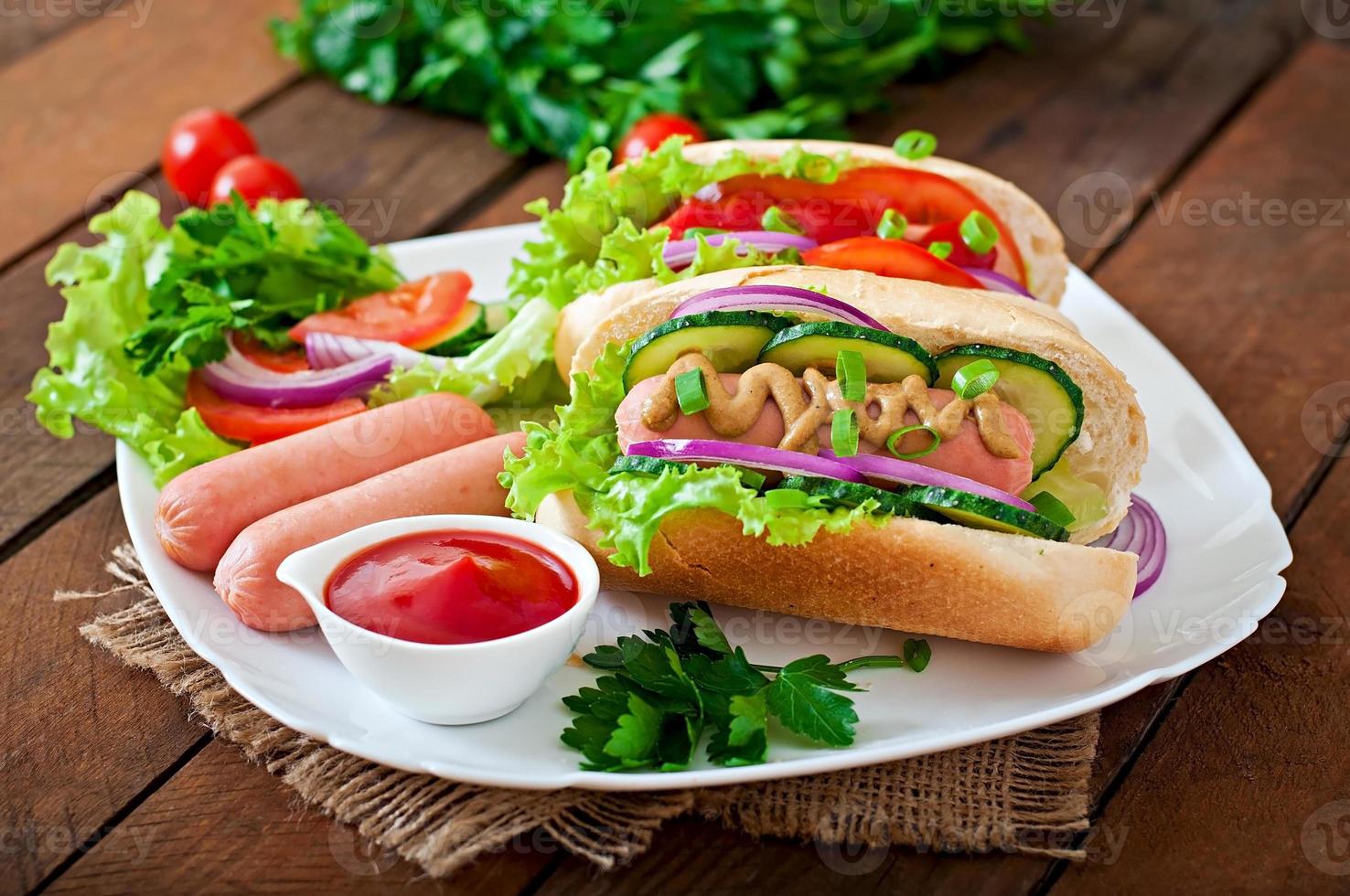 Hot Dog con salsa de tomate, mostaza, lechuga y verduras en la mesa de madera foto
