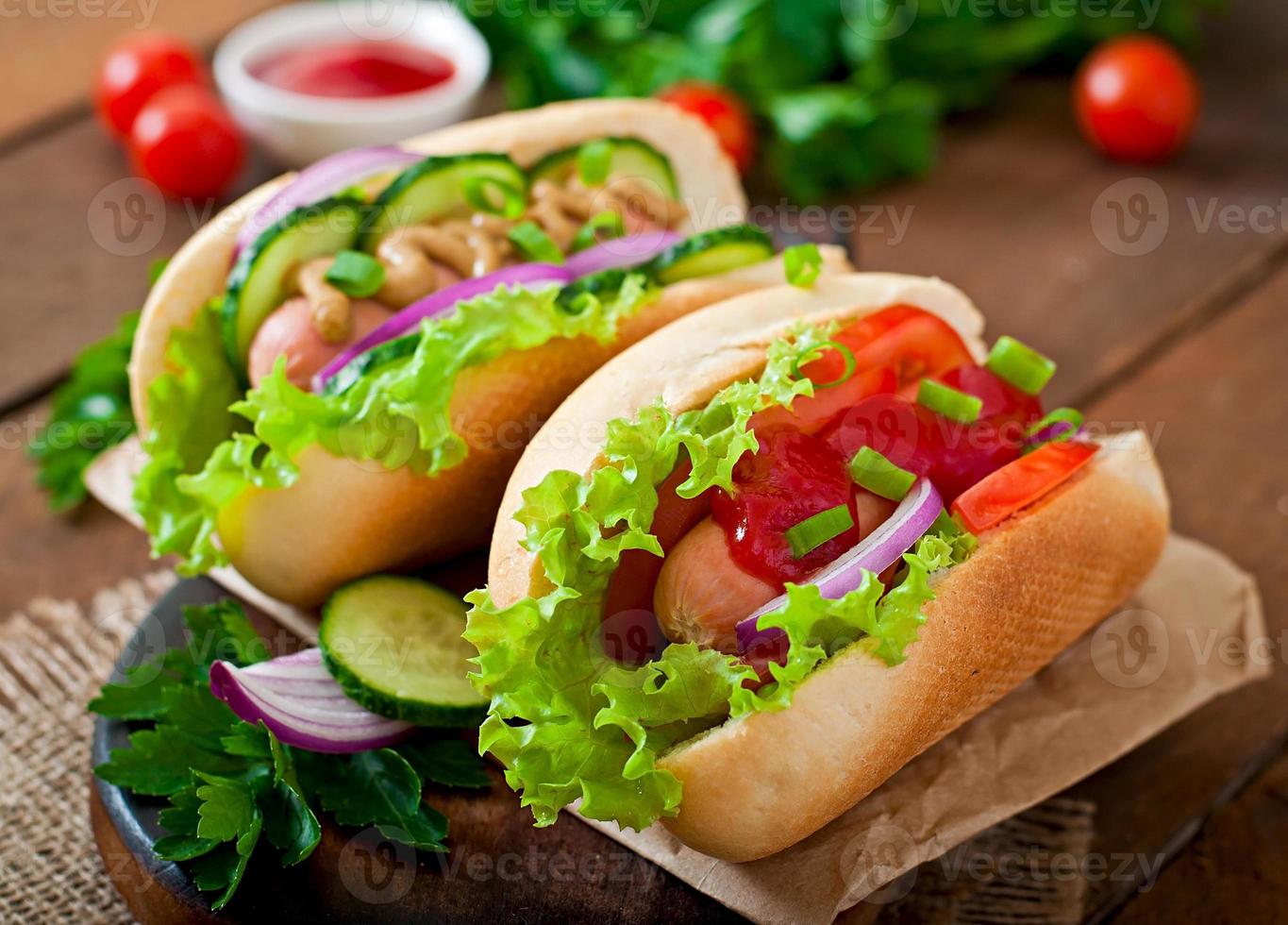 Hot Dog con salsa de tomate, mostaza, lechuga y verduras en la mesa de madera foto
