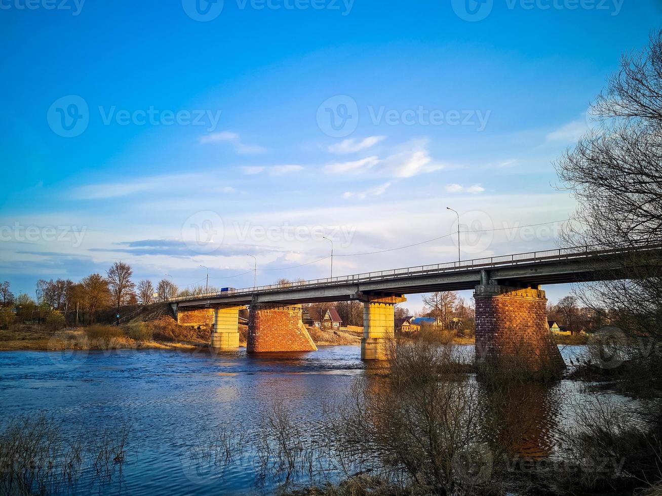 Ancient bridge over the river with stone pillars. Rapid flow of water in spring. Sunset view. photo