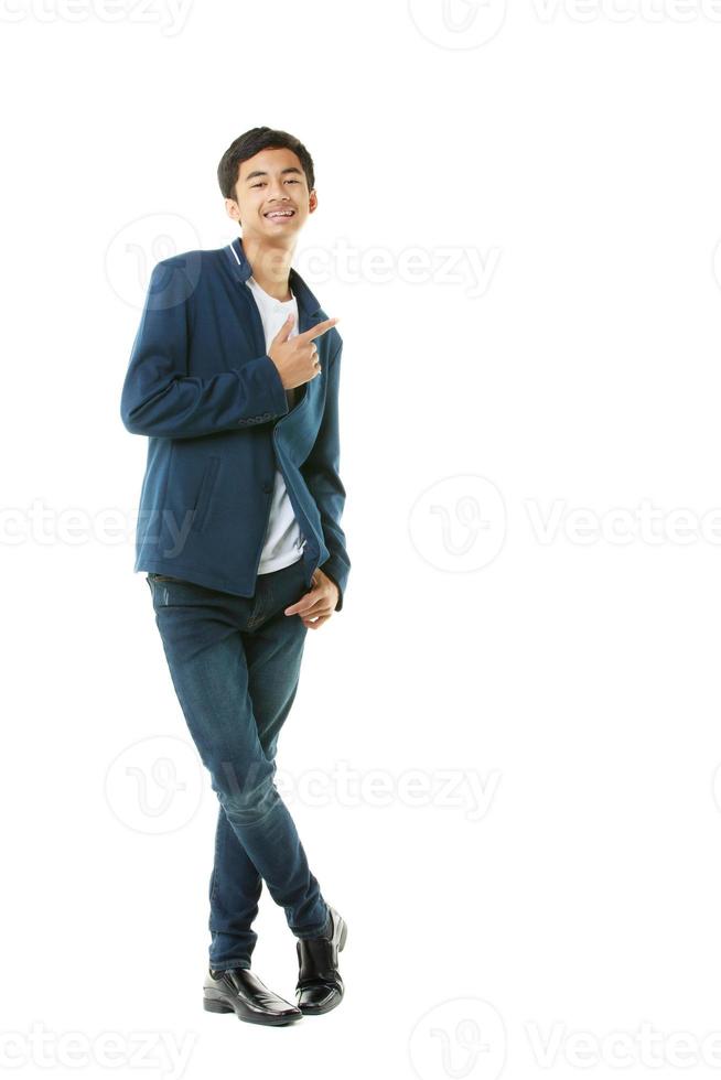 Asian early teenage boy in casual wear with braces is smiling self-assuredly, pointing his finger at isolate space on white background. photo