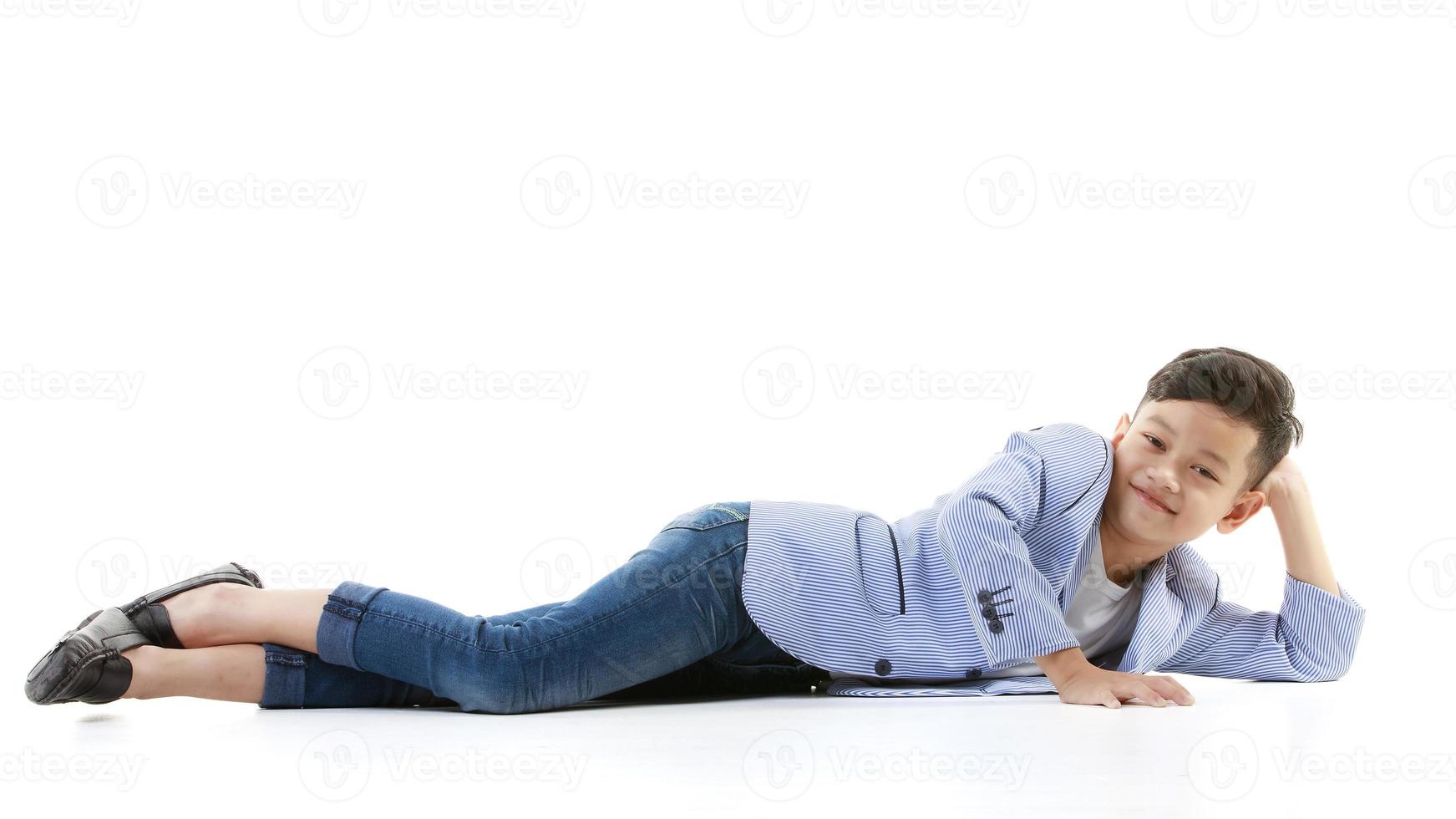 un niño asiático de 10 años con una chaqueta informal está tirado en el suelo y sonriendo alegremente de buen humor mirando la cámara. conceptos positivos para los estilos de vida de niños y hombres jóvenes. foto