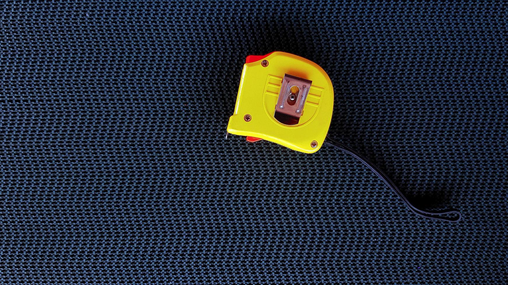Yellow Tape measure on black conveyor belt background with copy space on left. Tool for measure distance of object and size or dimension. photo