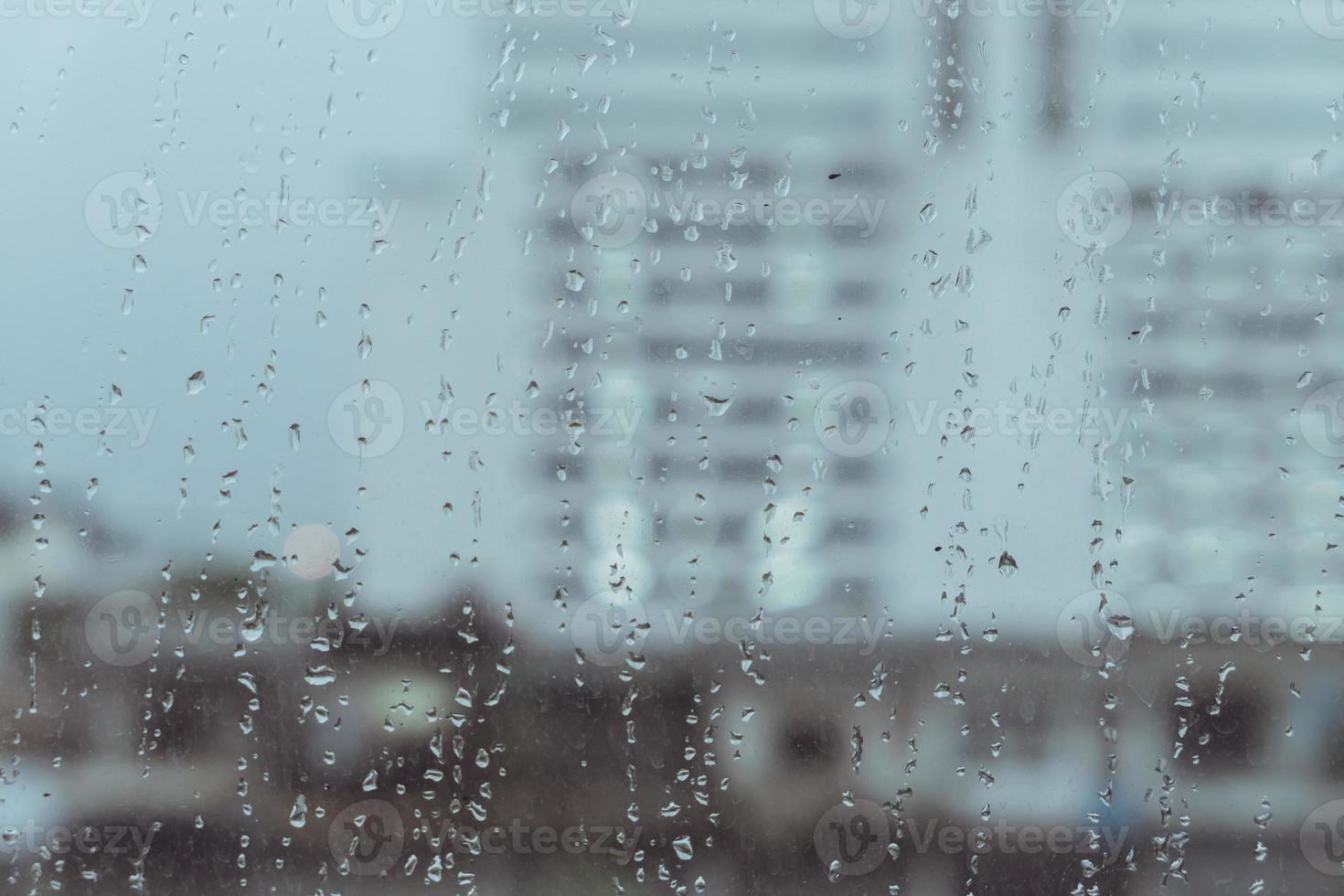 lloviendo en el cristal de las ventanas con el fondo del edificio de la ciudad borrosa foto