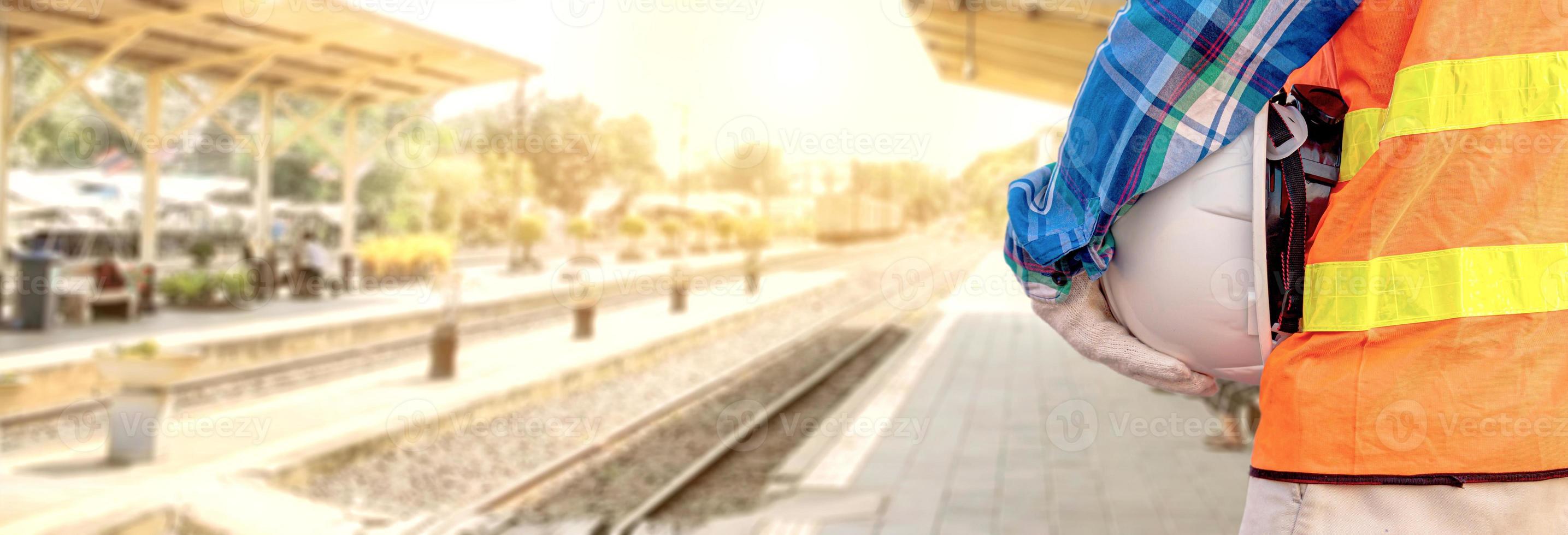 An engineer or foreman holding a helmet in a safety vest stands at the train station. photo