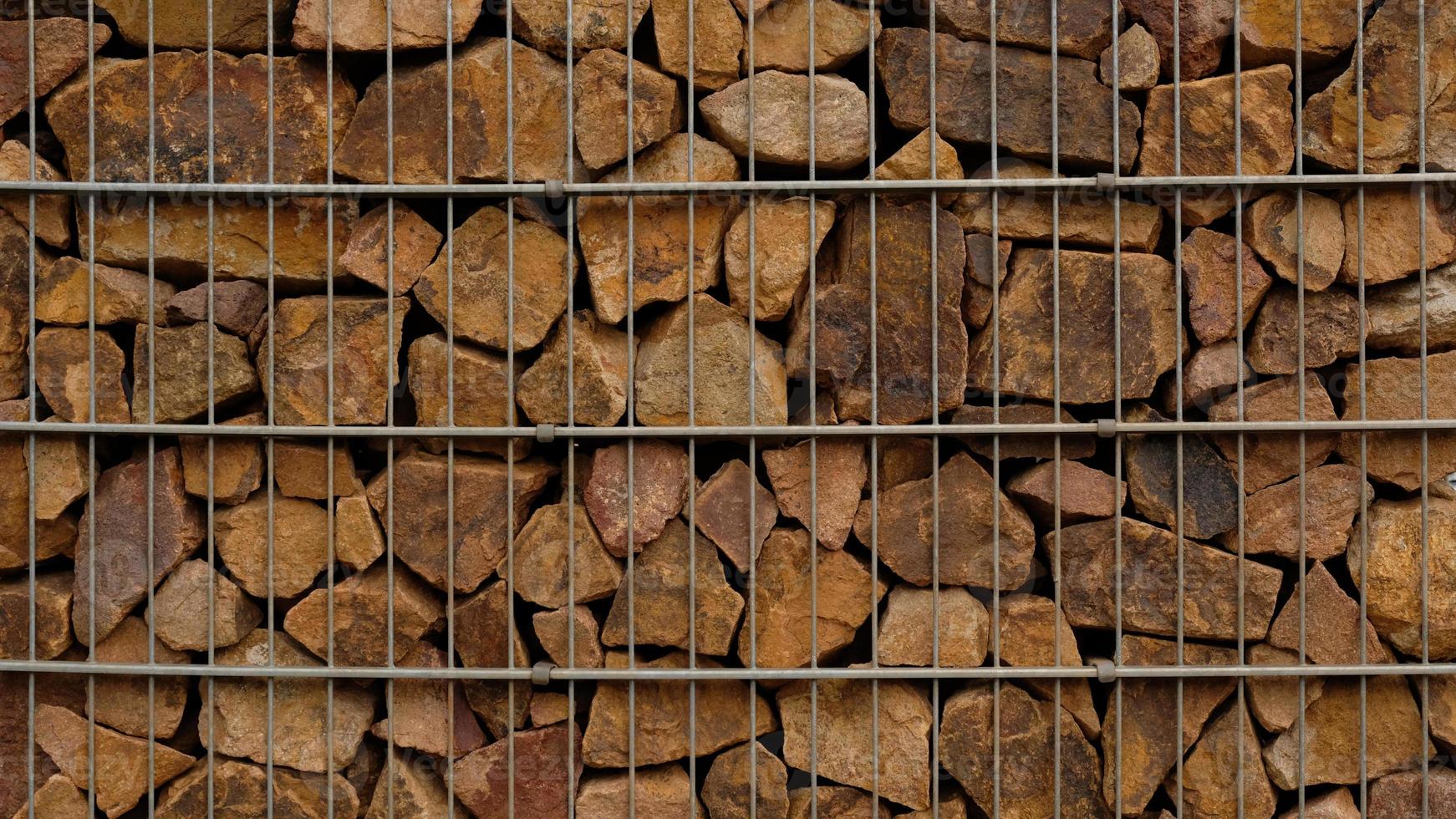 Muro de contención de gaviones: piedras marrones de primer plano en cestas metálicas de gaviones mantenidas por el muro de contención. pared protectora de gaviones rellenos de piedras y atados con alambre de metal grueso. diseño con textura de pared ecológica. foto