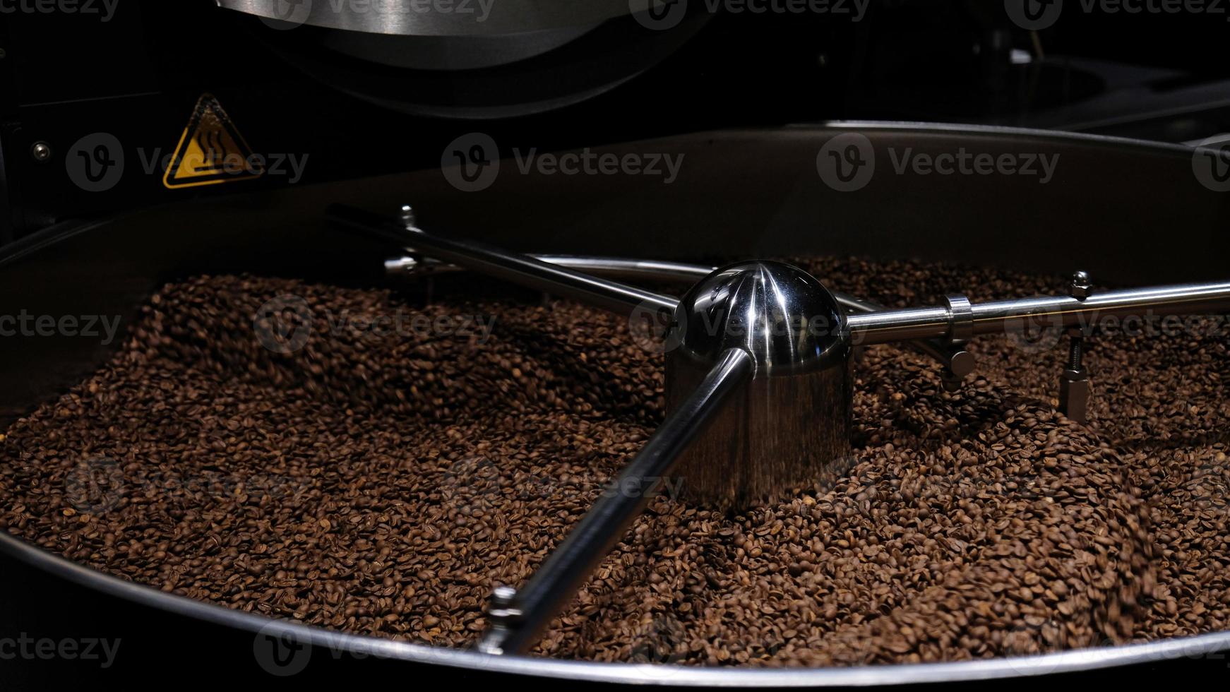 Coffee roaster machine at coffee roasting process. Mixing coffee beans. Roasted spinning cooler professional machines and fresh brown coffee beans movement close-up dark photo at factory.