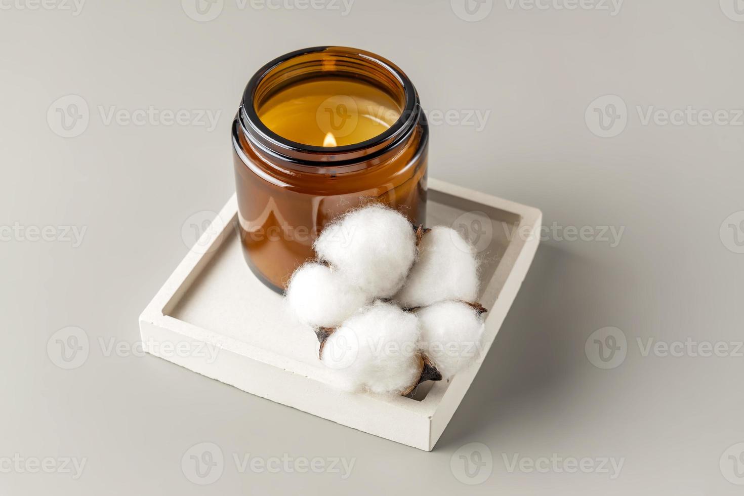 Natural wax candle in brown glass jar with cotton flower on concrete tray. Minimalism, mmockup. coxy style photo