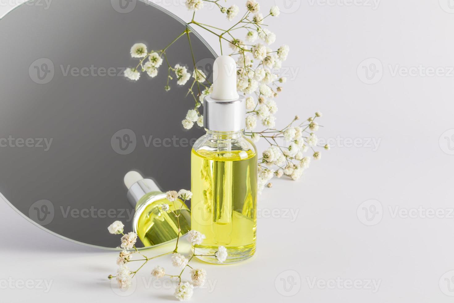 una botella de vidrio con una pipeta se refleja en un espejo redondo con una gypsophila. vista frontal. fondo pastel Presentación de un producto cosmético. foto