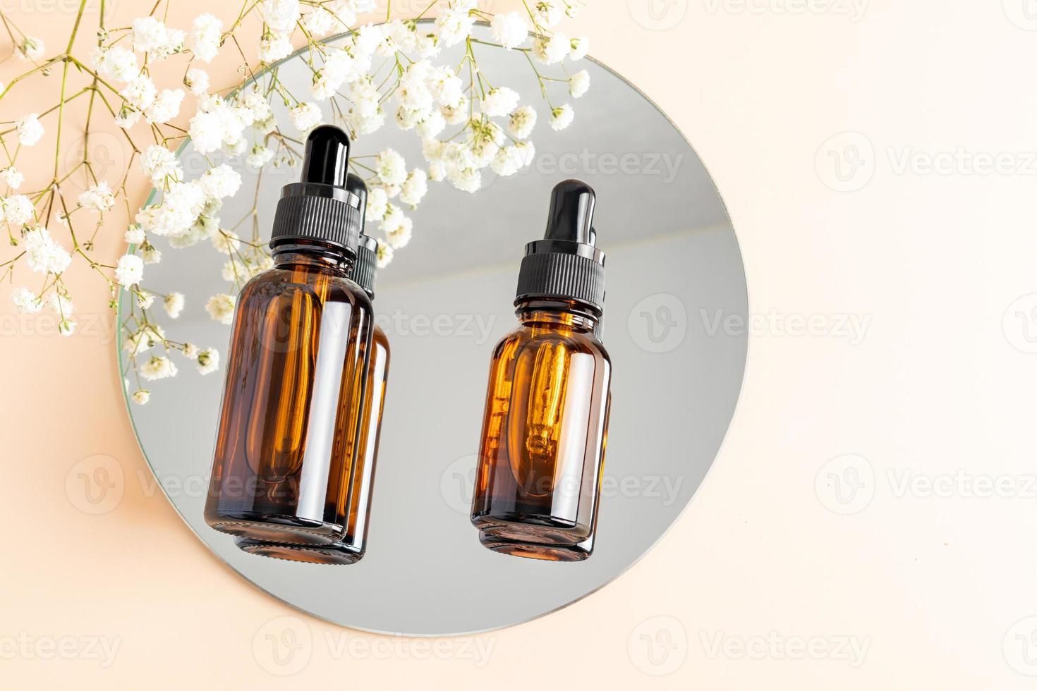 Two cosmetic bottles with a pipette lie on a round mirror. reflection in the mirror. top view. eco-natural facial skin care products. photo