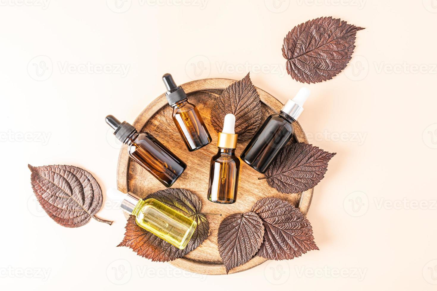 a set of glass bottles with a pipette with a natural organic remedy on a brown wooden tray among the autumn leaves. top view. beige background. photo