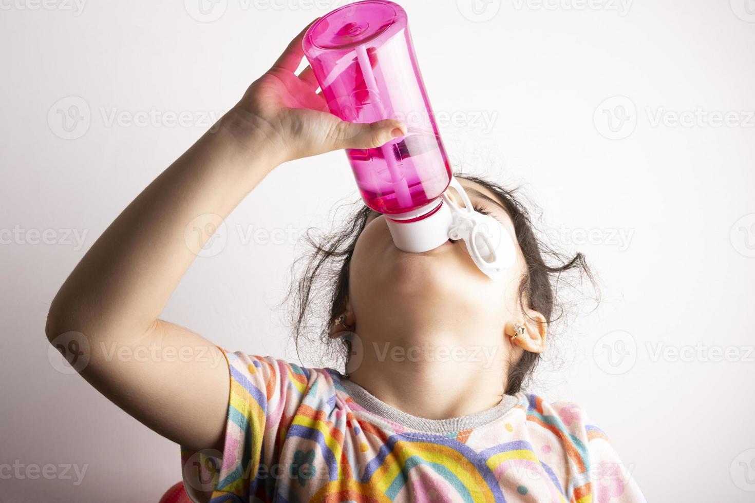 Little girl drinking water from rised bottle photo