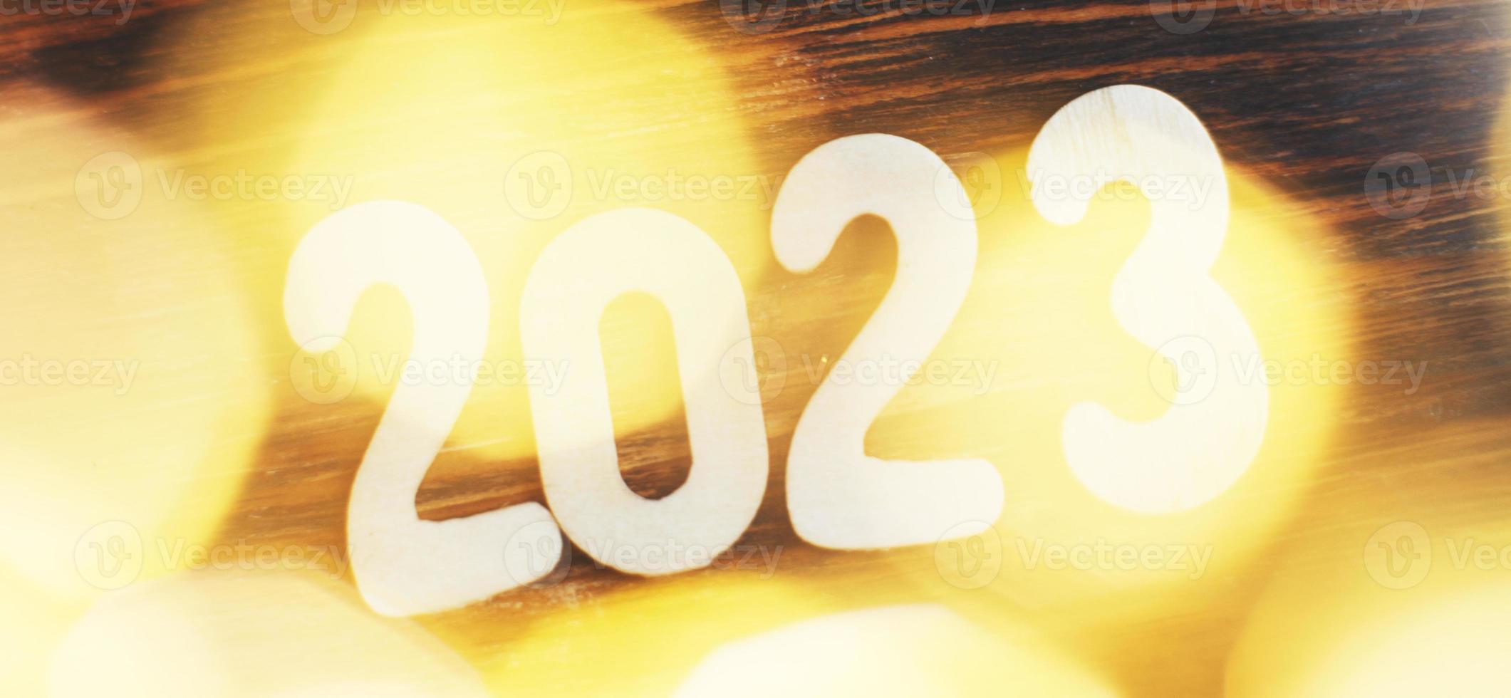 wooden number 2023 on christmas beautifull shiny gold background. sparkle festive blurred bokeh photo