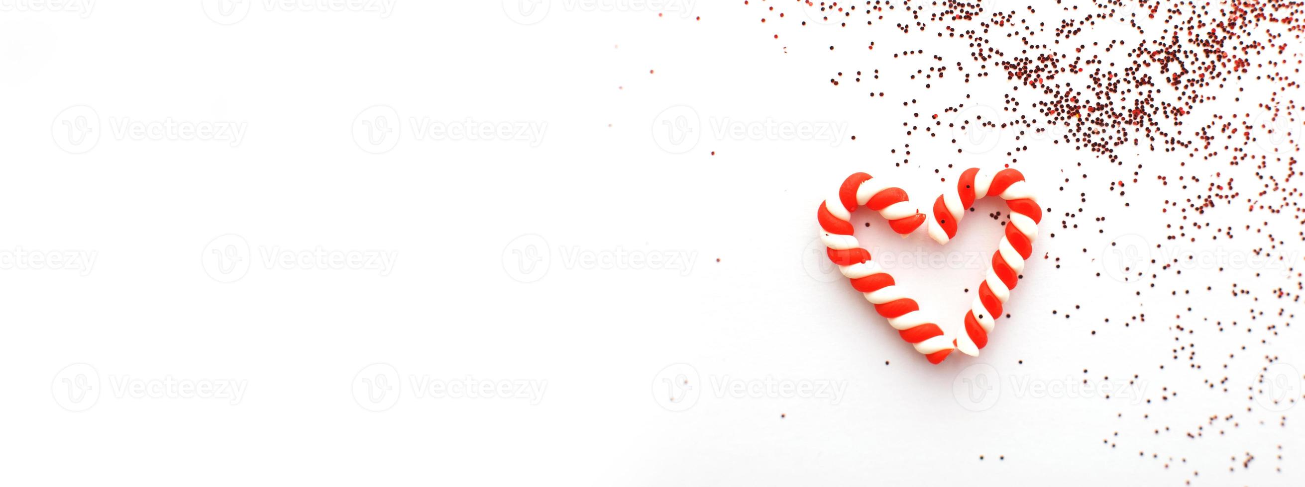 Christmas composition with candy canes in form oh heart on blue wooden background with red sequins photo