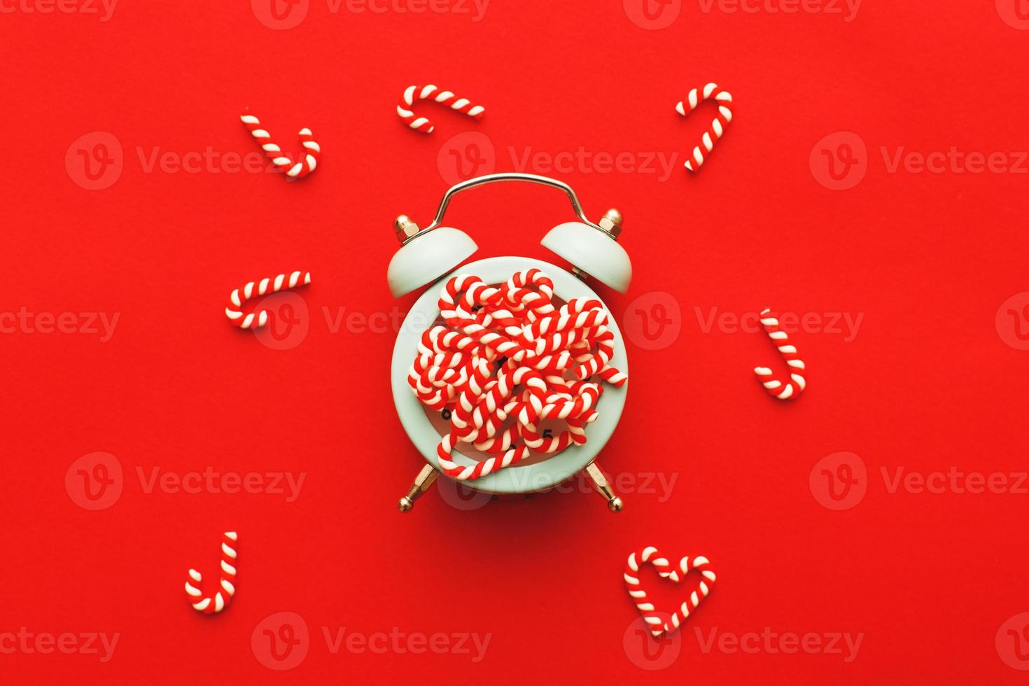 Christmas background with candy canes on alarm clock on red background photo