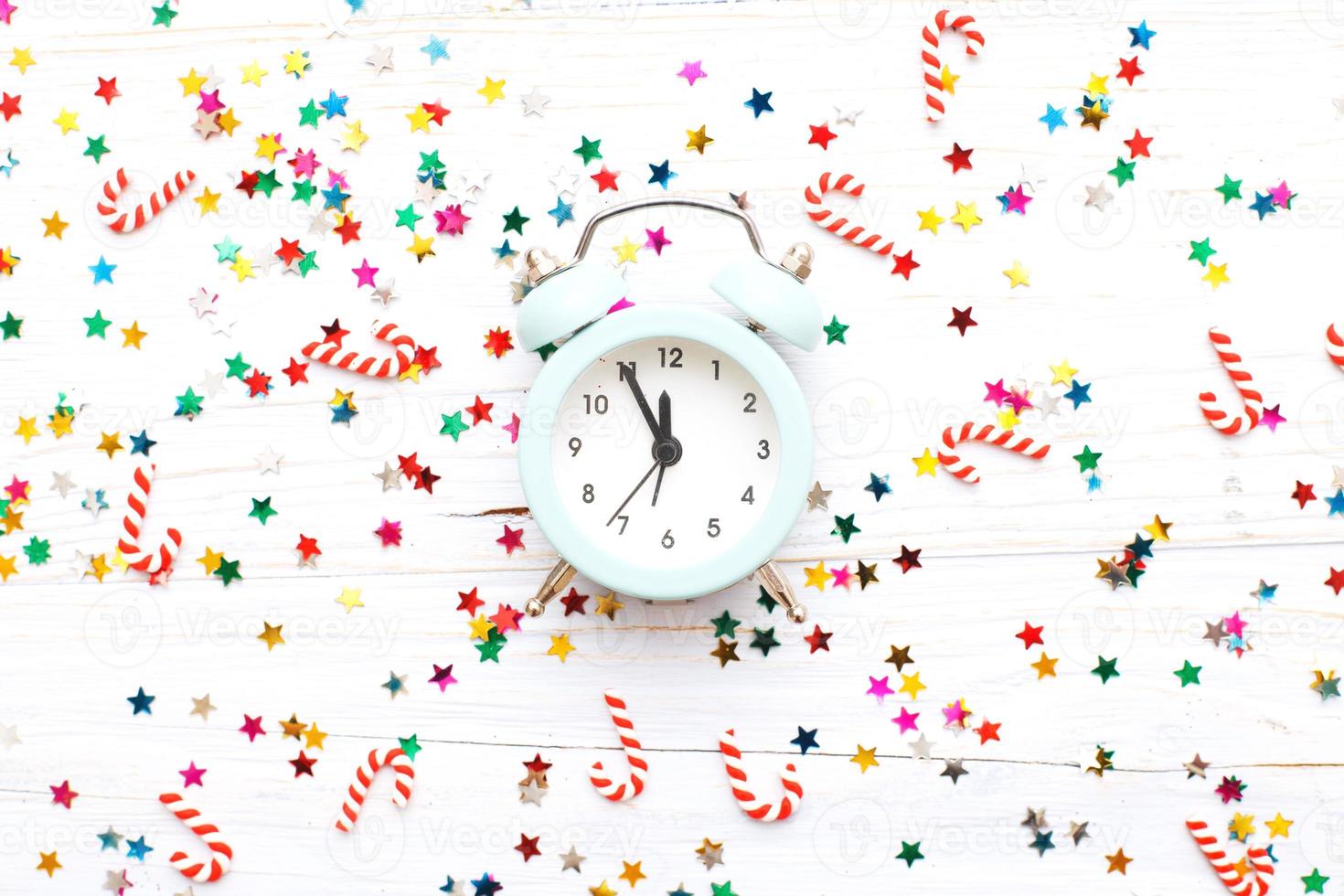 Christmas background with candy canes with alarm clock and multicolored sequins on wooden background photo