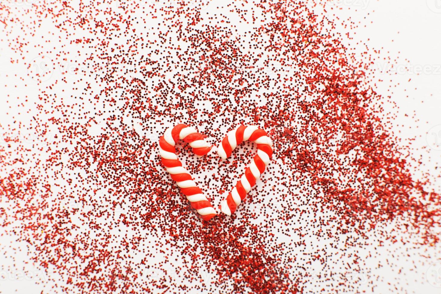 Christmas composition with candy canes in form oh heart on blue wooden background with red sequins photo