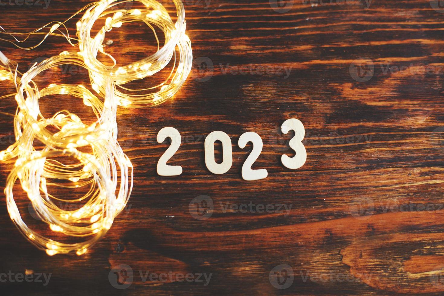wooden number 2023 on christmas shiny wooden background. with sparkle festive gold garland photo